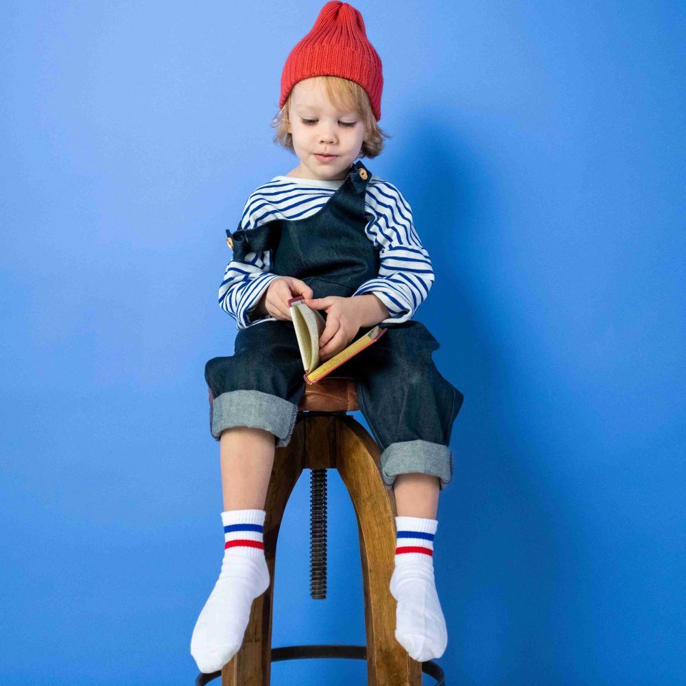 Happy Cranio Ausbildung - Kleinkind-Schulkind - Sitzendes Kind mit roter Mütze und Latzhose